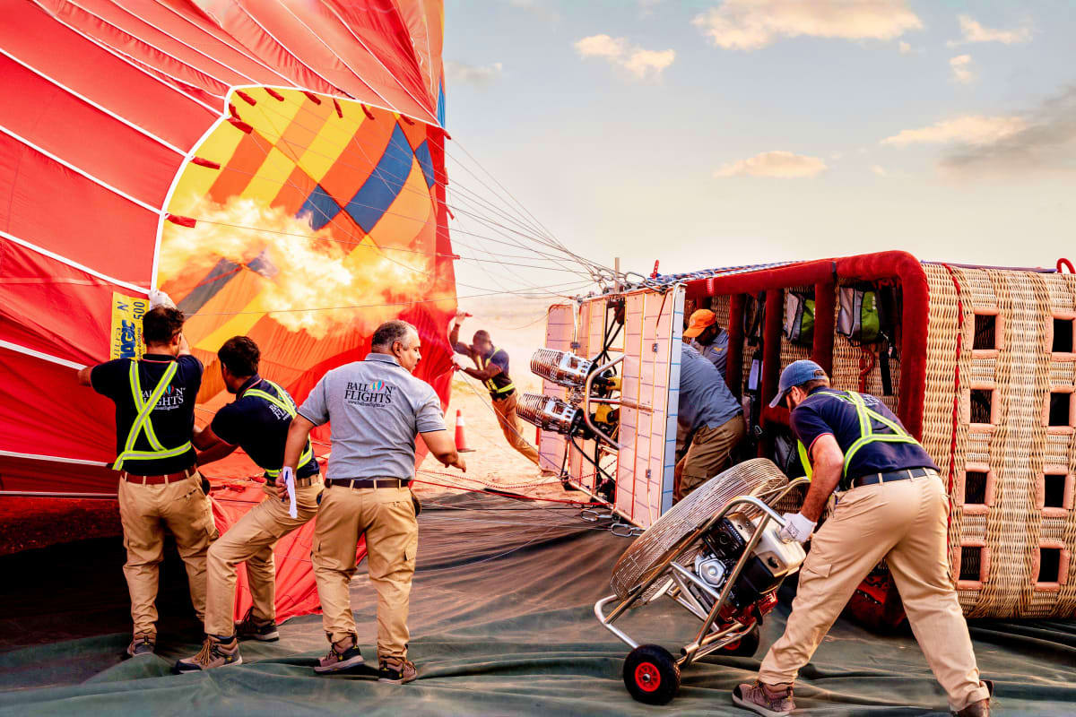 Hot air balloon crew members in safety vests preparing a large red and yellow balloon for flight at dawn in Dubai desert