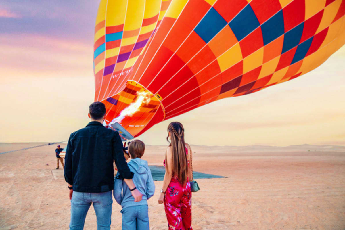 Family watching colorful hot air balloon being inflated on beach at sunrise in Dubai desert