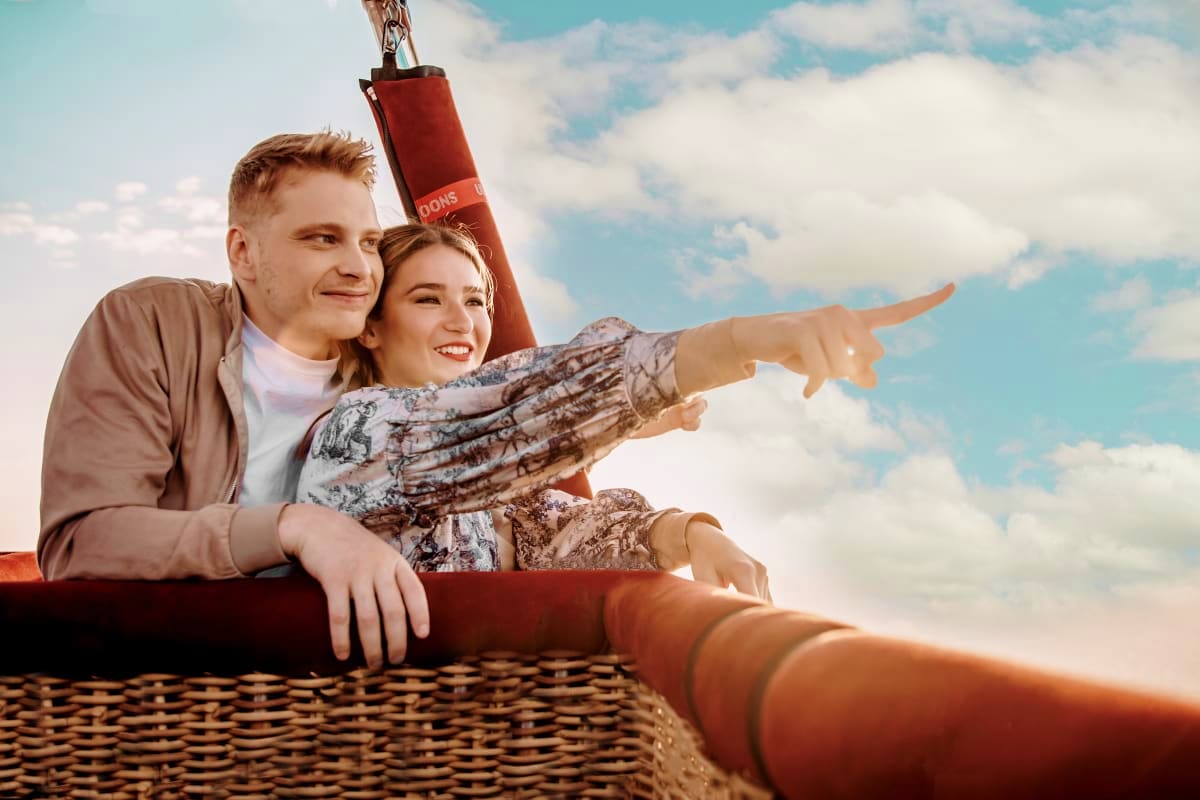 Couple in hot air balloon basket pointing toward horizon with cloudy sky background during Dubai balloon flight experience