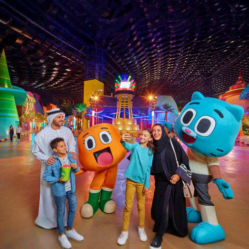 Family posing with colorful cartoon character mascots inside IMG Worlds of Adventure indoor theme park with illuminated attra