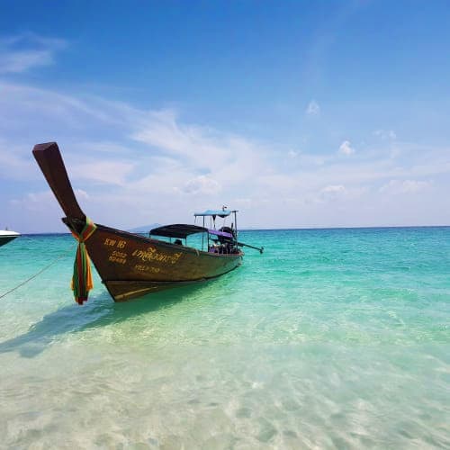 Traditional wooden long tail boat anchored in turquoise shallow water at James Bond Island, Thailand