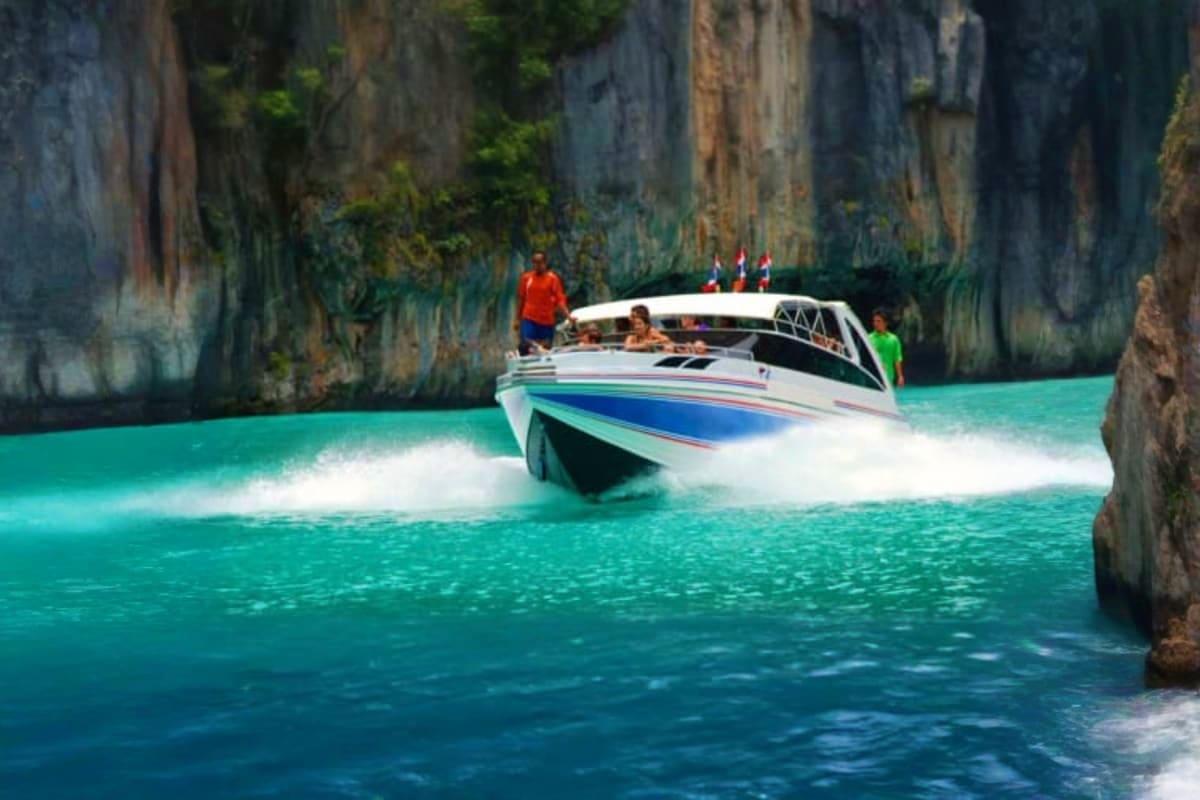 Speed boat with tourists navigating turquoise waters near towering limestone cliffs at James Bond Island, Thailand