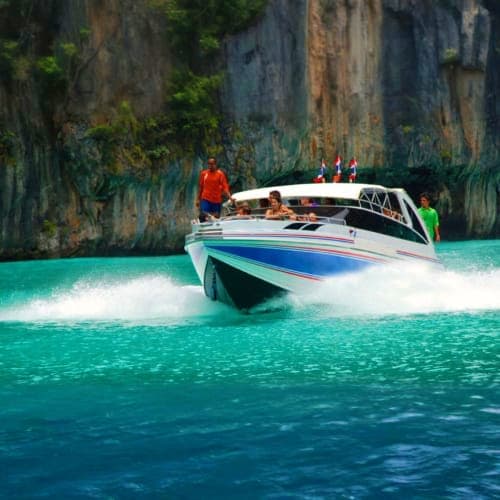Speed boat with tourists approaching tall limestone cliffs at James Bond Island in turquoise tropical waters