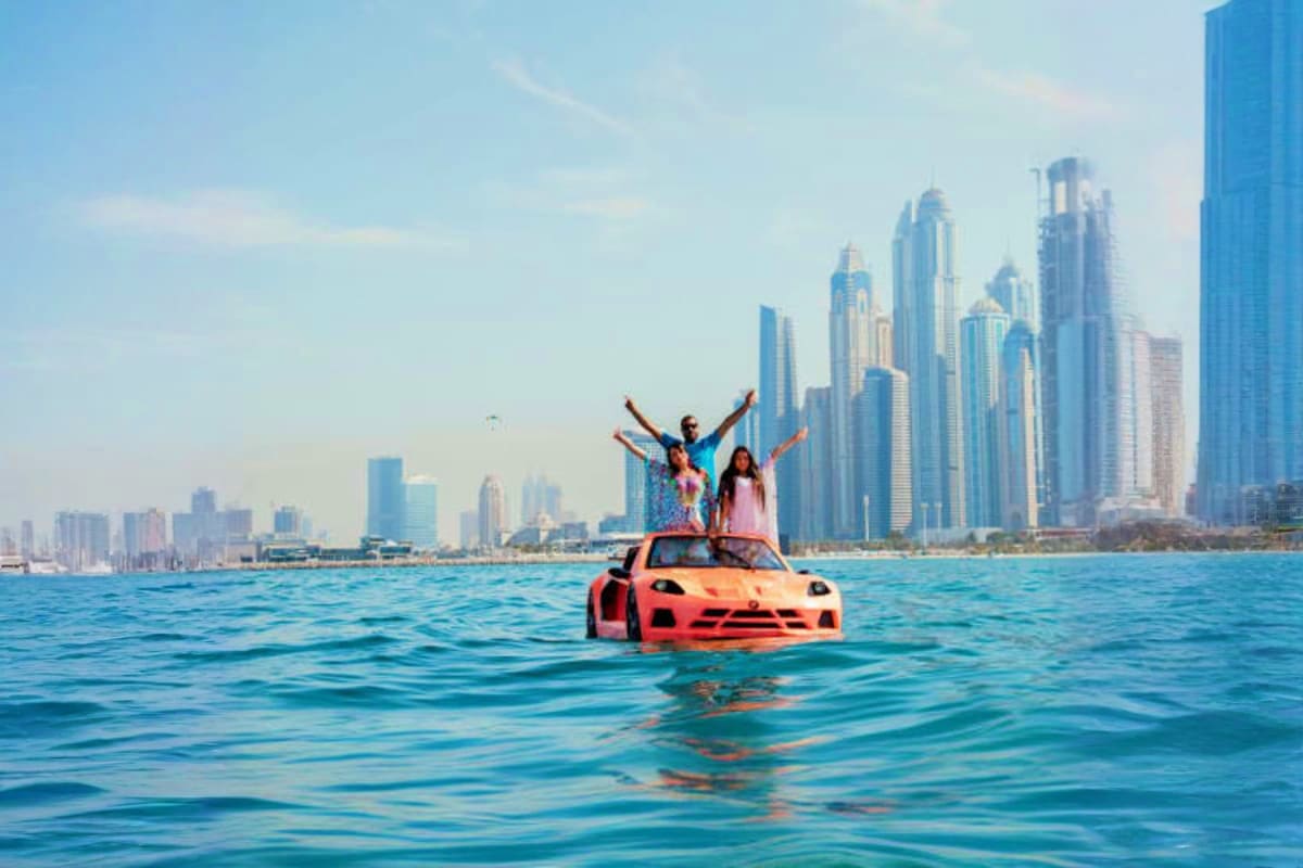People celebrating on a red sports car floating in turquoise water with Dubai skyline in the background
