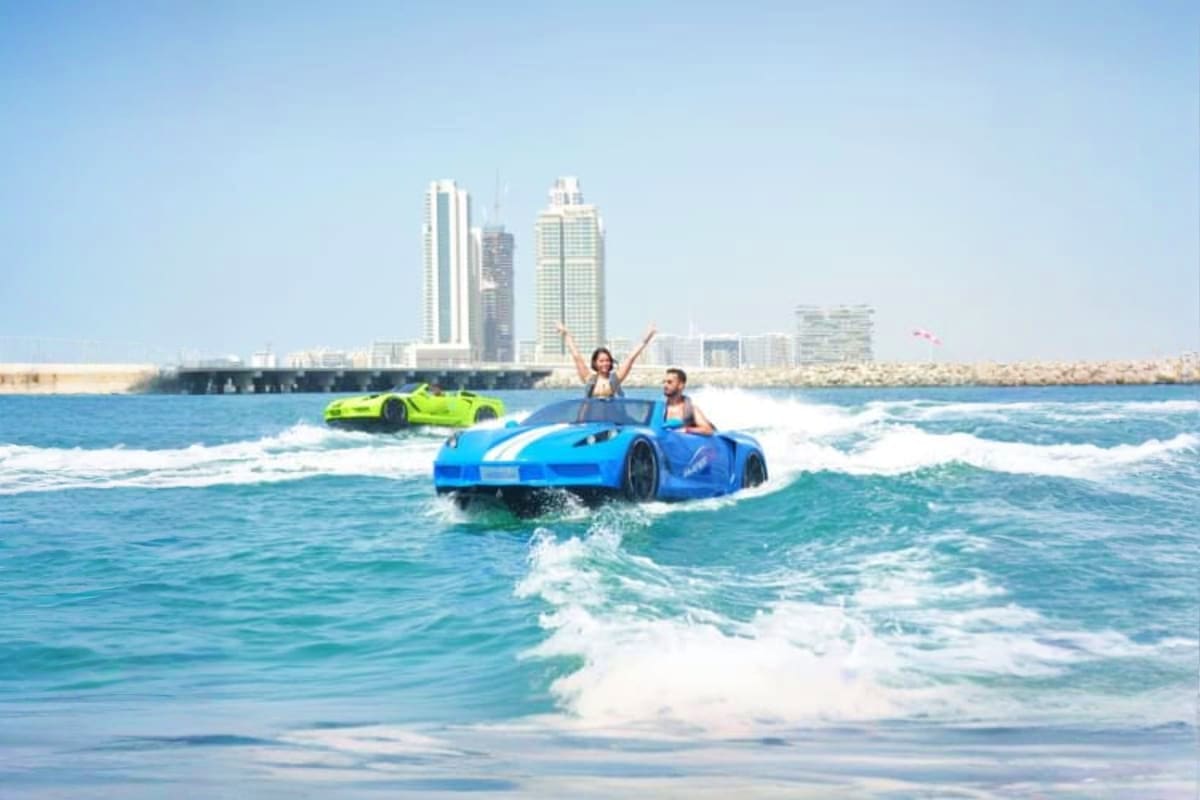 Couple enjoying a blue jet car in ocean waves with Dubai skyline and high-rise buildings visible in background