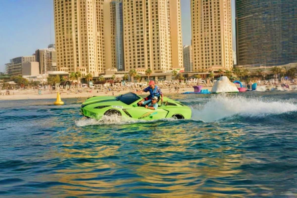 Jet Car Activities Dubai Person riding bright green amphibious jet car in Dubai waters with high-rise hotels and sandy beach in background