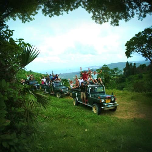 Tourist jeeps lined up on grassy terrain with tropical vegetation and mountain valley views during jungle safari tour