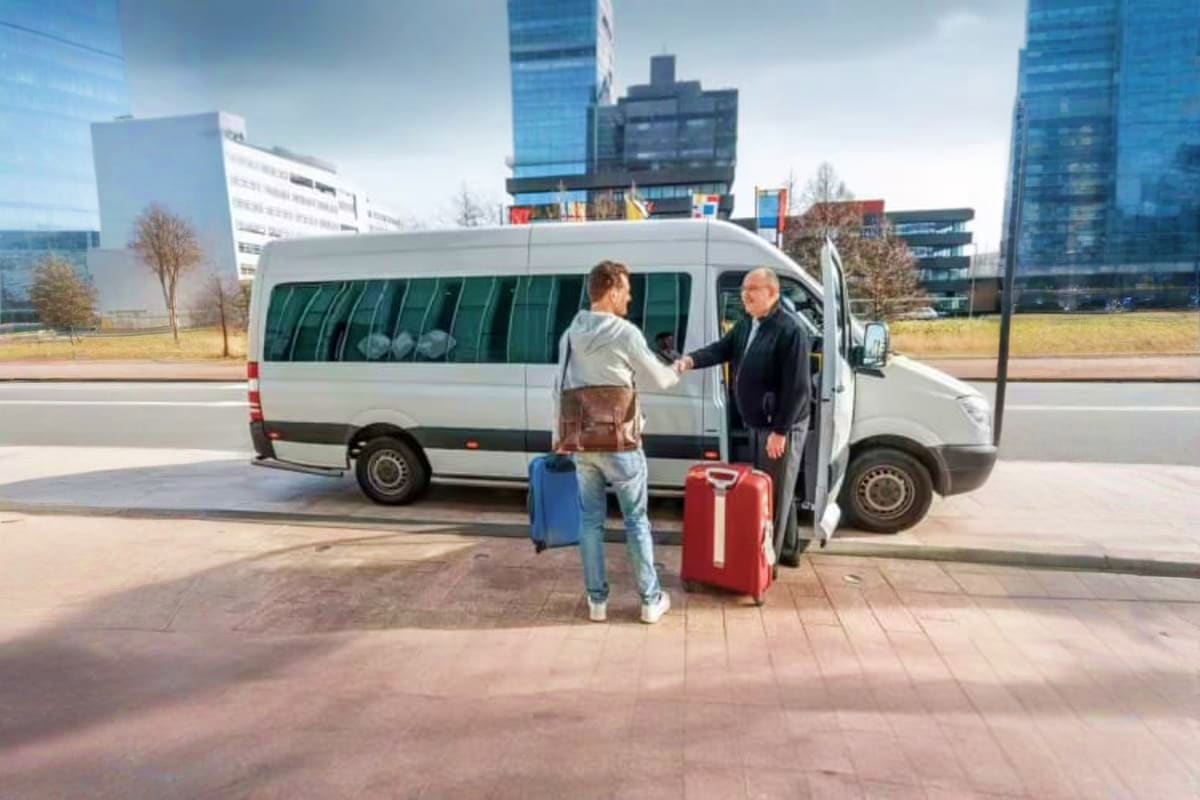 Passenger boarding white minivan with luggage for intercity transfer service in modern city setting with skyscrapers