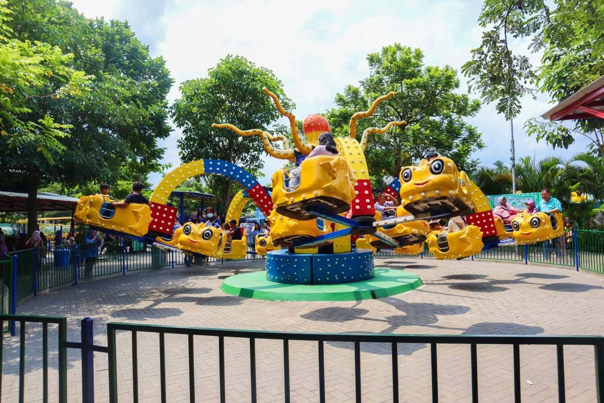 Colorful yellow octopus-themed spinning ride with orange tentacles at Legoland Malaysia theme park, surrounded by green trees