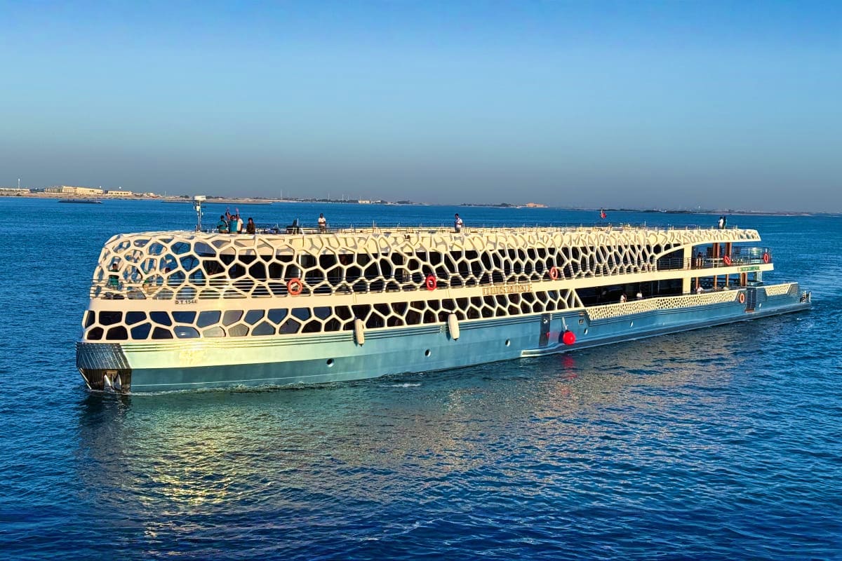 Lotus Mega Yacht Dinner Cruise Modern luxury cruise ship with distinctive honeycomb pattern design anchored in clear blue waters off a coastal town