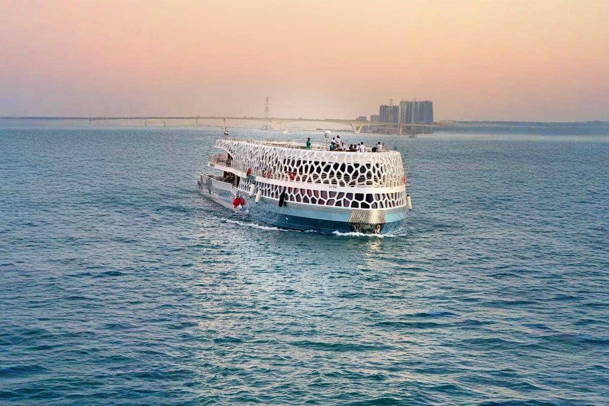 Modern white mega yacht with distinctive patterned exterior sailing in blue sea at dusk with coastal city skyline in backgrou