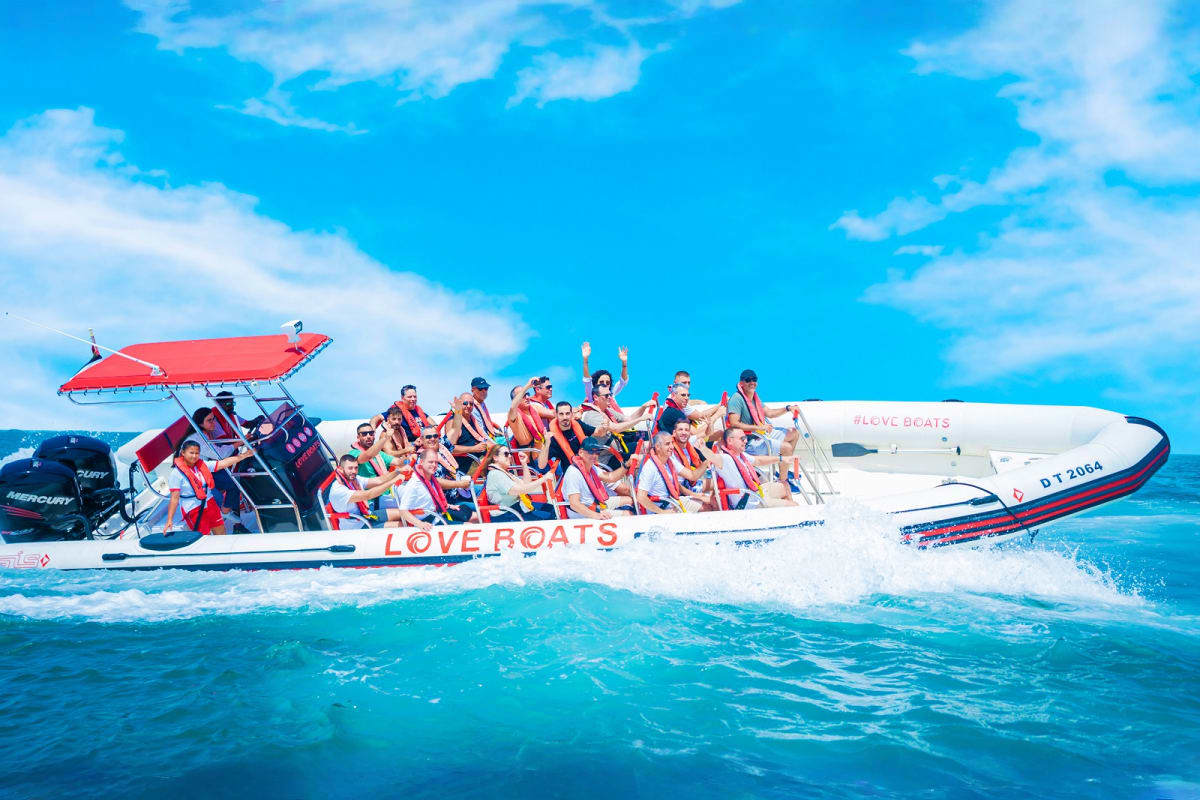 Large group of tourists on white and red Love Boats speedboat in turquoise Arabian Gulf waters under blue sky