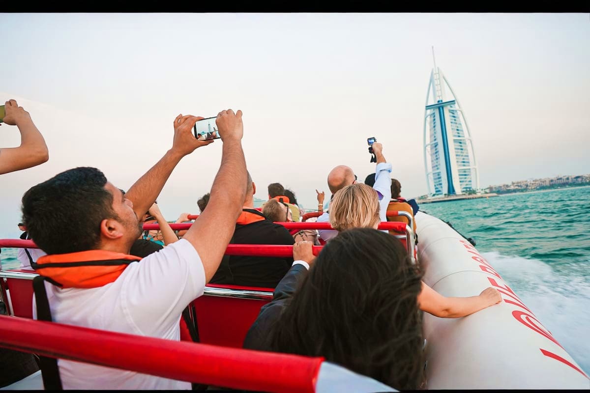 Tourists on a red speedboat taking photos of the Burj Al Arab sail-shaped hotel in Dubai waters