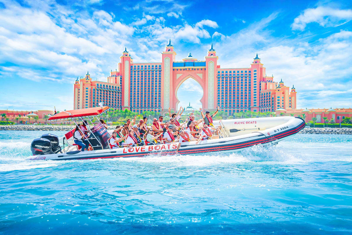 Speed boat full of tourists racing through blue water with Atlantis The Palm hotel in background, Dubai