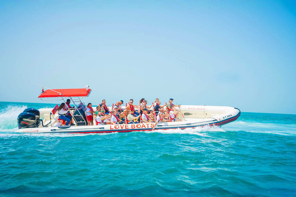Speedboat full of tourists wearing life jackets cruising through turquoise waters with red canopy in Dubai