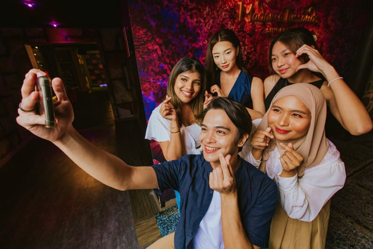 Group of five young people taking a selfie at a nightclub with colorful neon red and blue lighting in the background
