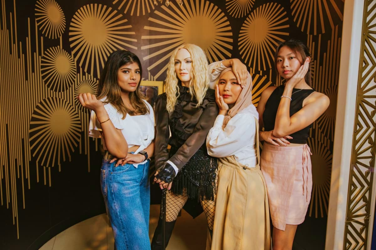 Four women posing together in front of gold starburst wallpaper at Madame Tussauds Singapore wax museum
