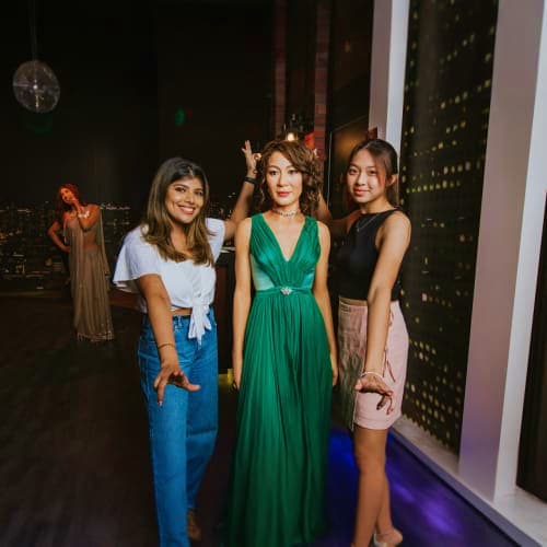Three women posing together at Madame Tussauds Singapore wax museum, with city skyline visible through windows behind them