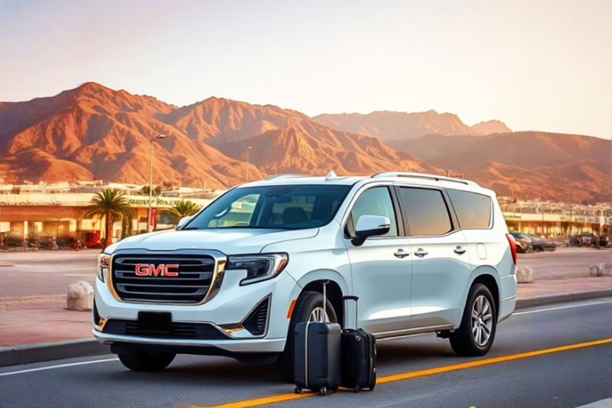 White GMC minivan with luggage on a desert road, mountains in background for Makkah to Madinah transfer service