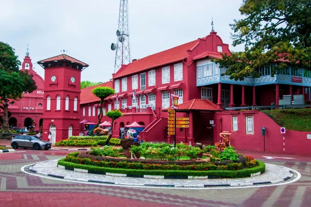 Historic red colonial buildings in Malacca town square with clock tower, landscaped gardens, and communication tower