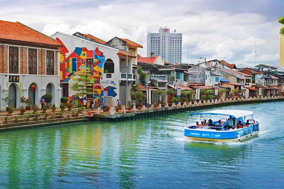 Blue tour boat cruising past colorful colonial buildings with street art along Malacca River waterfront