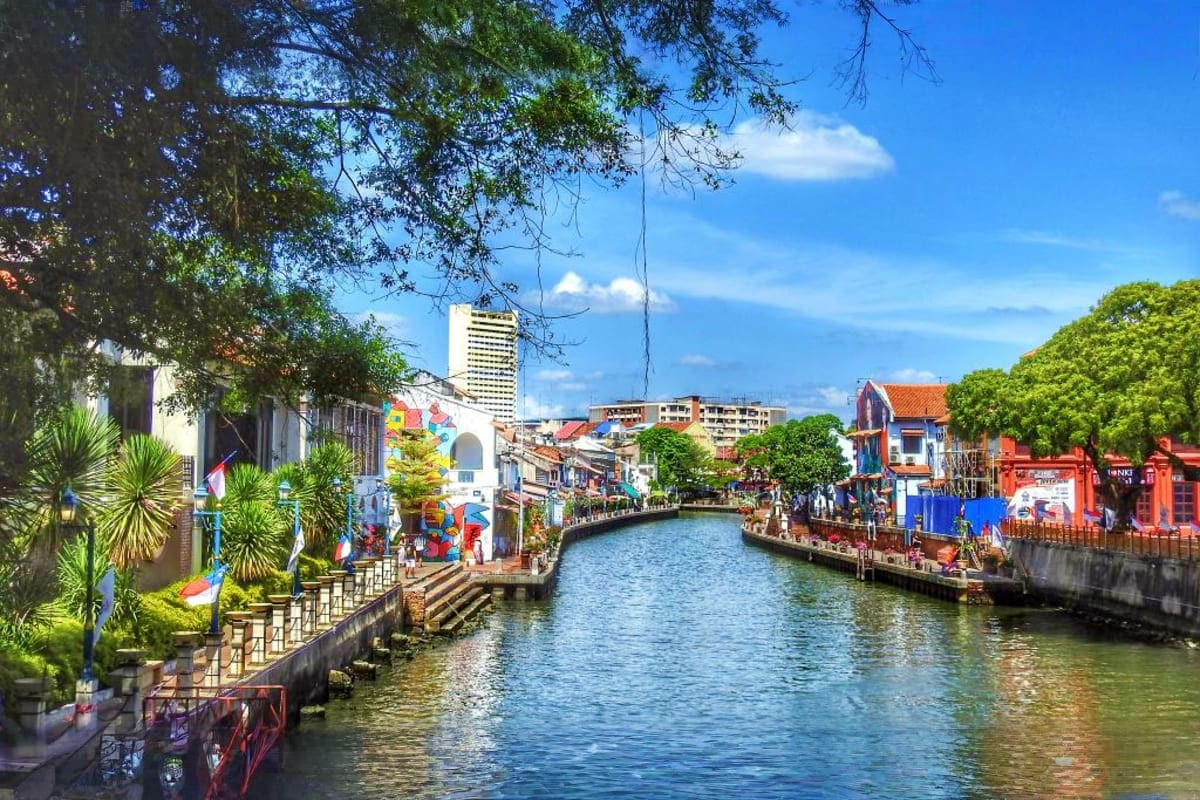 Malacca River with colorful historic buildings, street art, and palm trees lining the waterway under clear blue sky