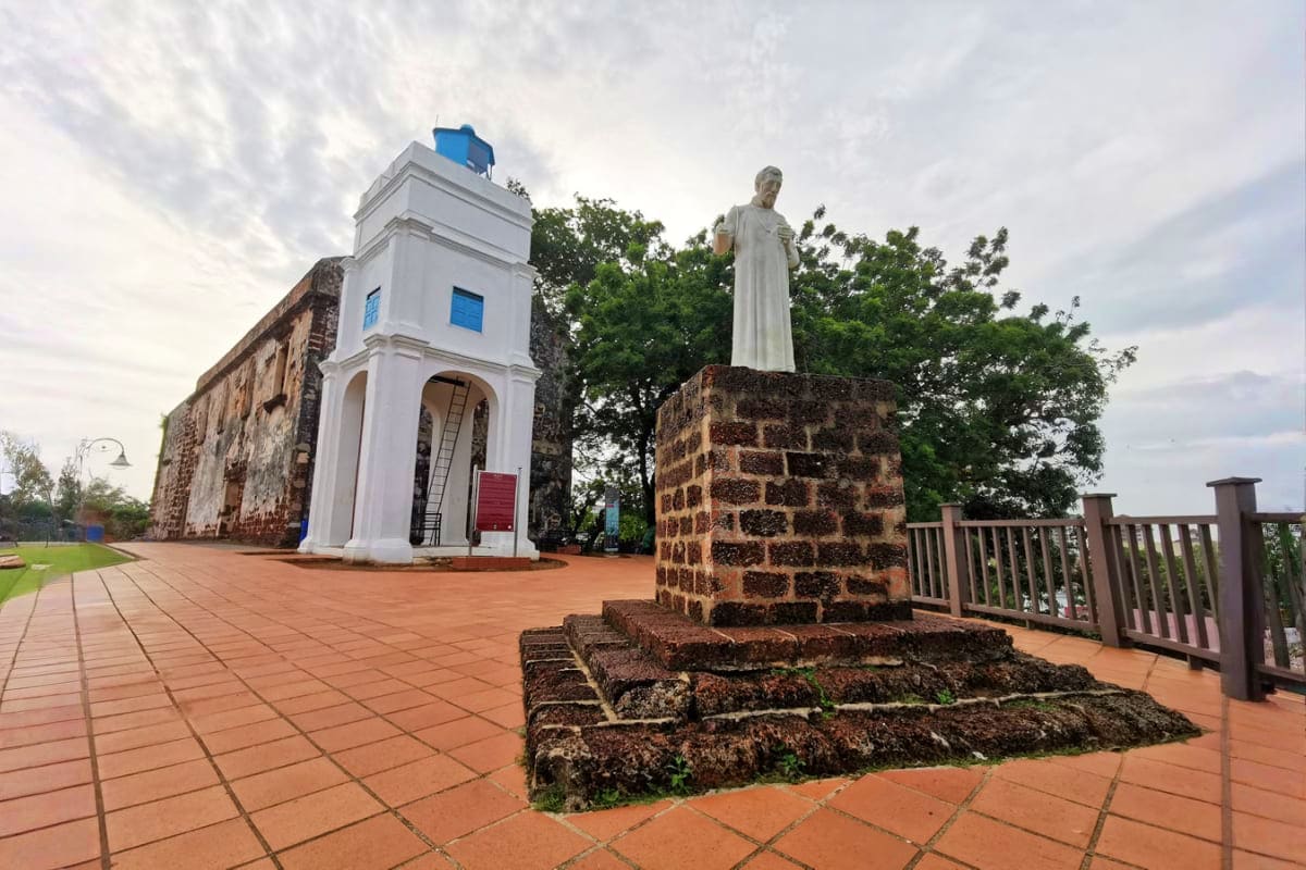 Historic stone ruins with white chapel tower and religious statue at A Famosa Fort in Malacca, Malaysia