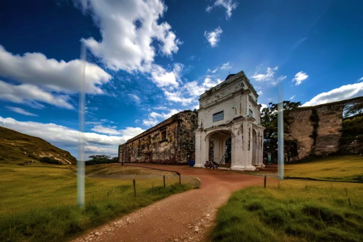 Historic ruins with white colonial structure and weathered stone buildings set in grassy landscape under blue sky