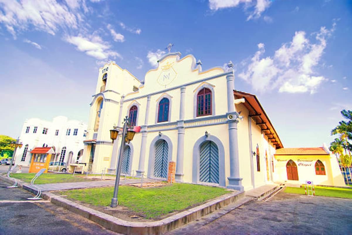 Historic cream-colored church with blue doors and arched windows under clear blue sky with white clouds