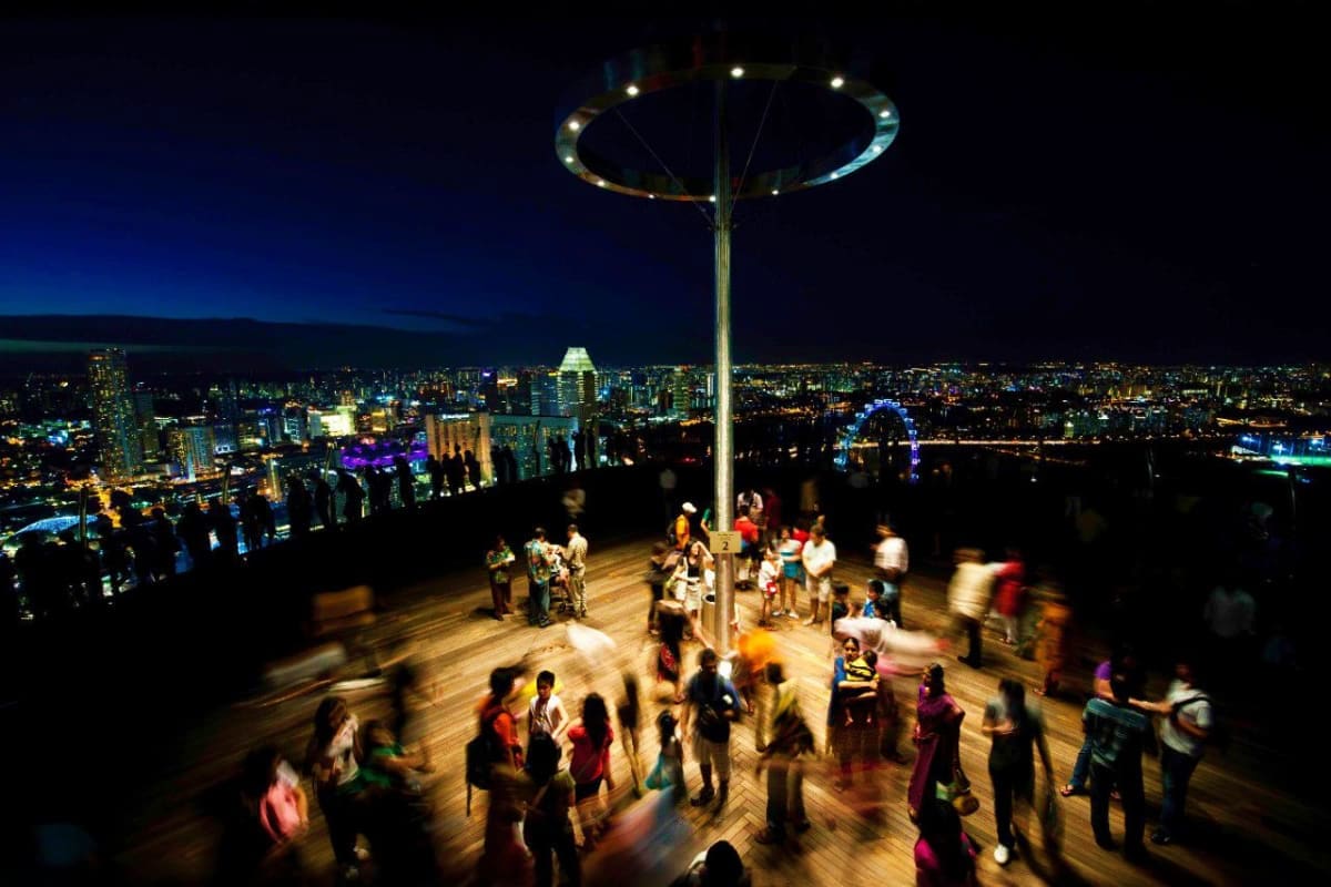 Visitors enjoying the illuminated observation deck at Marina Bay Sands with panoramic nighttime city skyline views in backgro