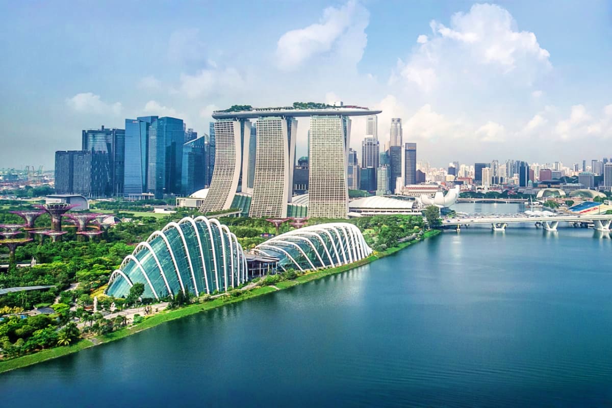 Aerial view of Marina Bay Sands hotel with iconic curved towers, Supertree Grove, and Singapore skyline reflected in blue wat