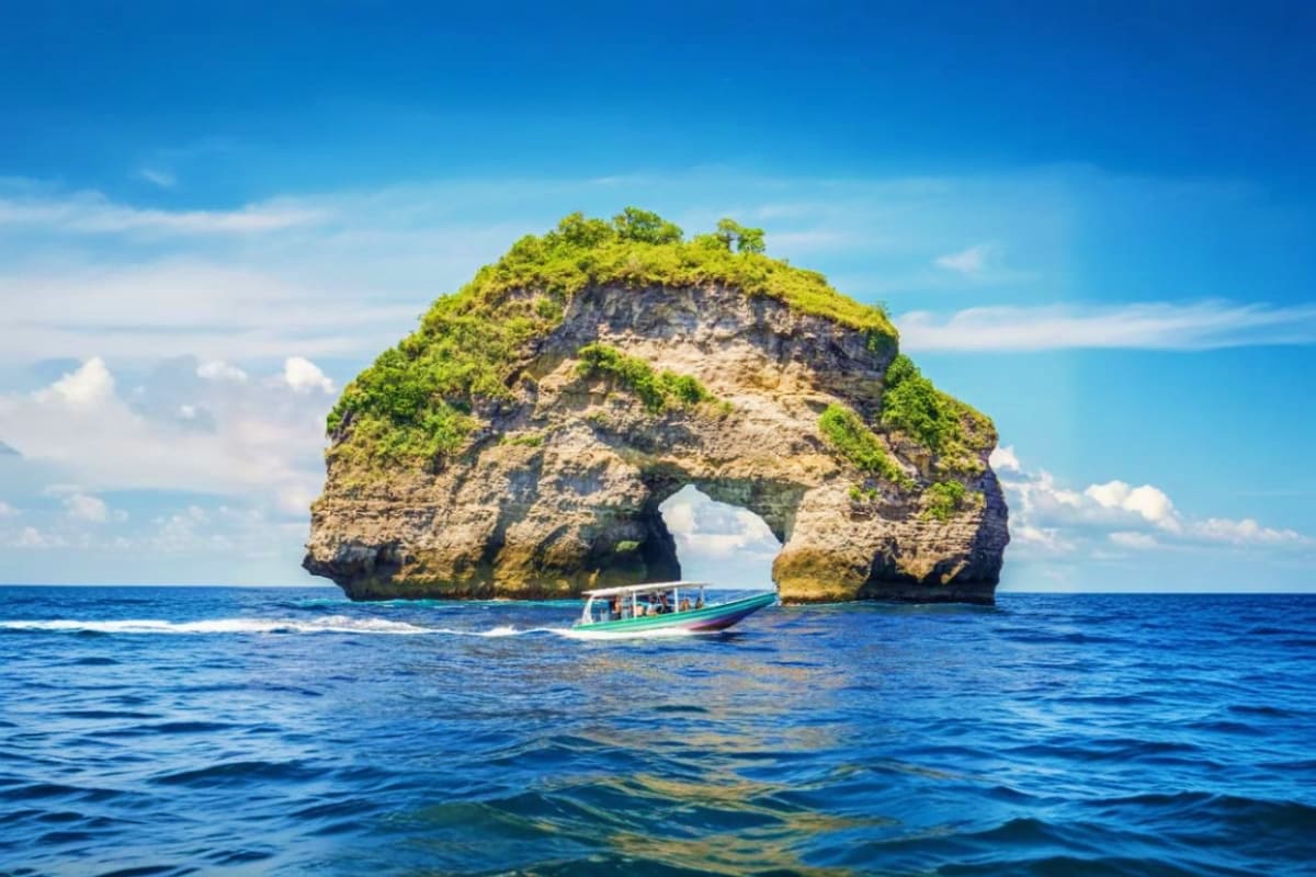 Nusa Penida Day Tour And Snorkeling Depart from Nusa Penida Tourist boat near Kelingking Beach's iconic natural rock arch formation in Nusa Penida, Bali surrounded by blue ocean water