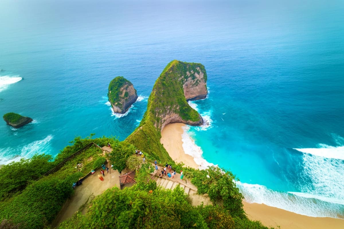 Aerial view of Kelingking Beach in Nusa Penida with distinctive T-Rex shaped cliff, turquoise ocean, and tourists at viewpoin