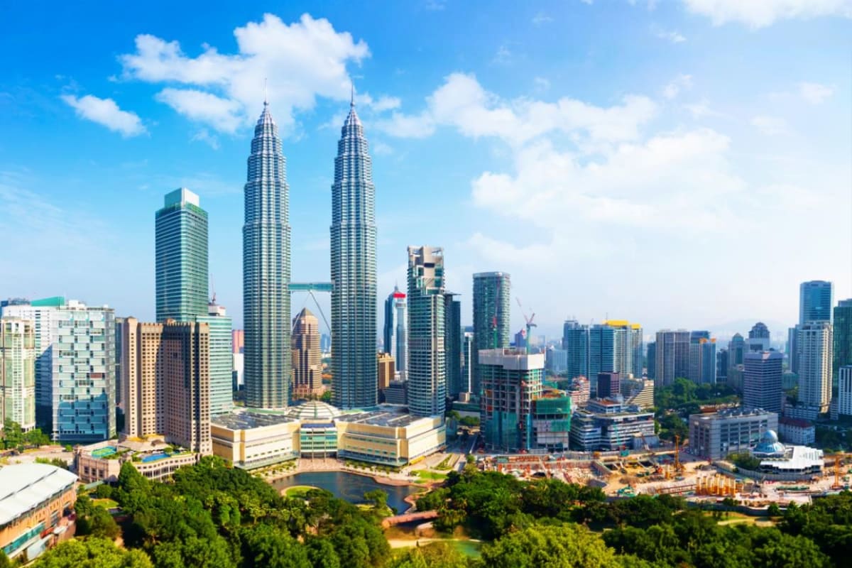 Petronas Twin Towers and Kuala Lumpur skyline with surrounding skyscrapers under blue sky with white clouds