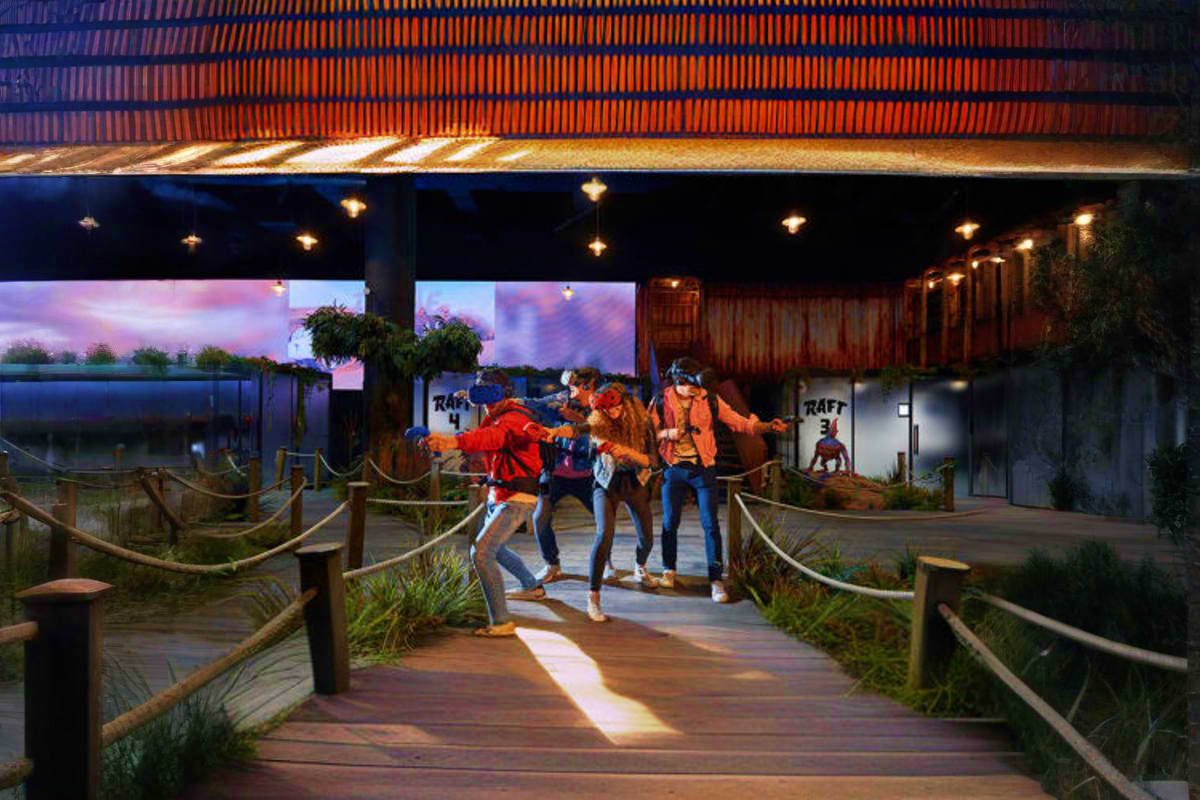 Play DXB Dubai Group of four people jumping on wooden boardwalk at sunset under modern orange corrugated roof structure at Play DXB Dubai