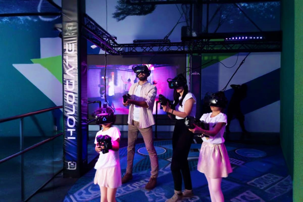 Play DXB Dubai Group of children and adults wearing VR headsets in a futuristic gaming arena with purple lighting and blue floors at Play DX