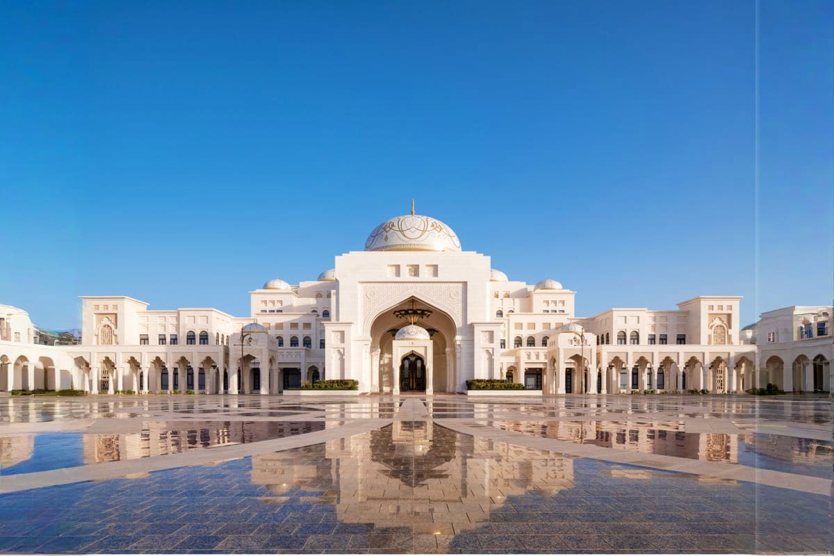 Qasr Al Watan palace in Abu Dhabi with white dome architecture reflected in wet courtyard plaza under clear blue sky