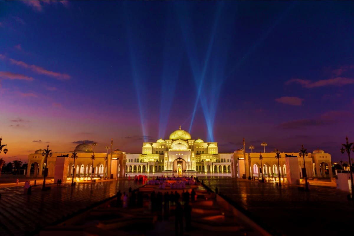 Qasr Al Watan Abu Dhabi Qasr Al Watan palace illuminated at dusk with dramatic blue searchlight beams, grand dome, and visitors in courtyard at sunse