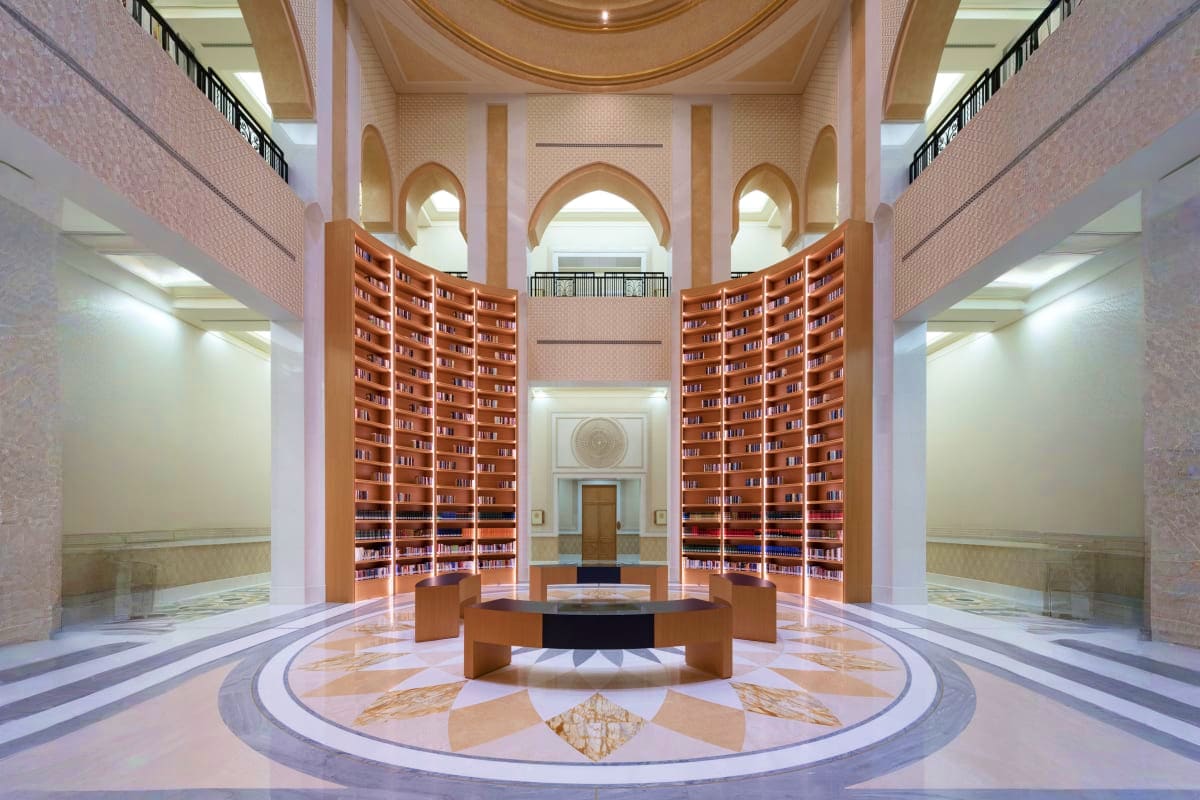 Modern library interior at Qasr Al Watan with symmetrical wooden bookshelves, arched windows, polished marble floors, and cen