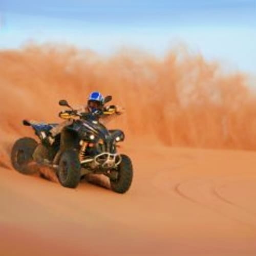 Quad Biking Abu Dhabi Person riding a yellow and black quad bike across sandy desert terrain with dunes in the background