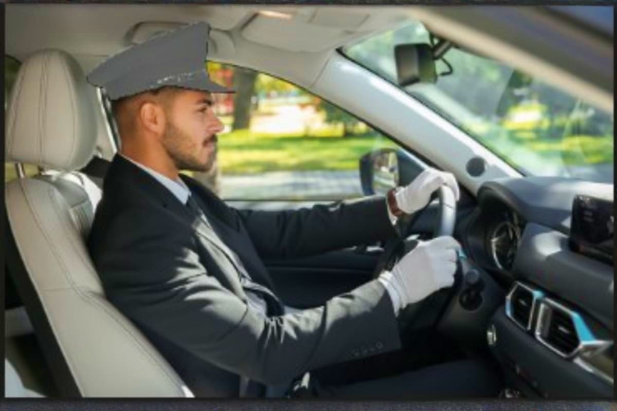 Man driving car wearing cap and white gloves, green landscape visible through windshield during daytime drive