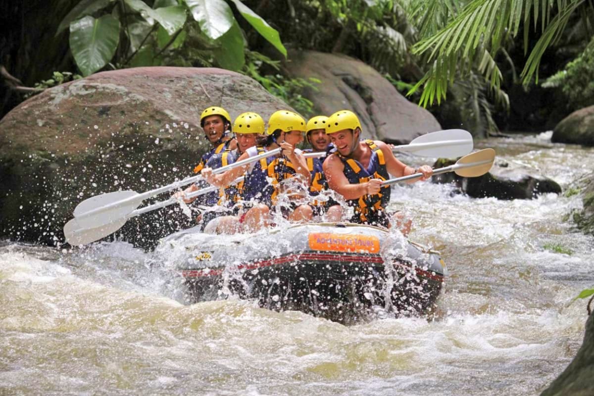 River Ayung Rafting and ATV Group of five people whitewater rafting on turbulent river in tropical jungle setting with large boulders and lush green vege
