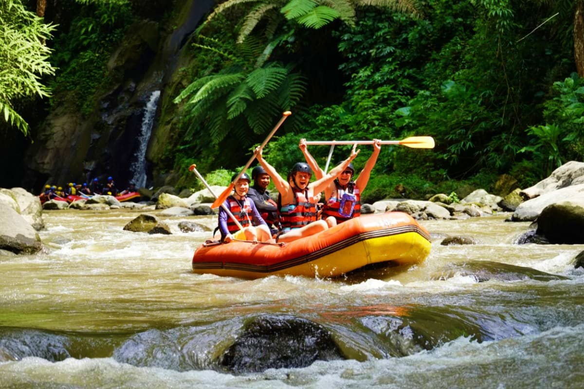 River Ayung Rafting and ATV Group of five people whitewater rafting on River Ayung in a red and yellow raft with paddles raised, surrounded by lush green