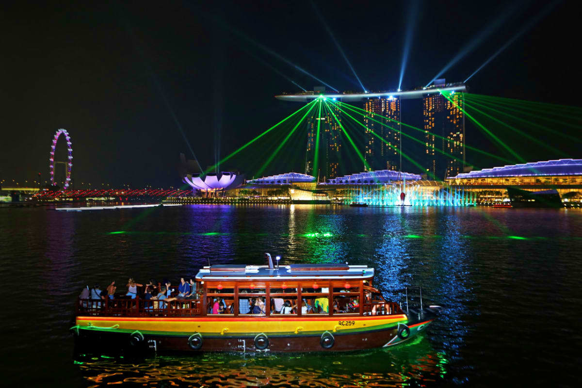 Colorful river cruise boat on Singapore River at night with Marina Bay Sands and green laser lights illuminating the skyline