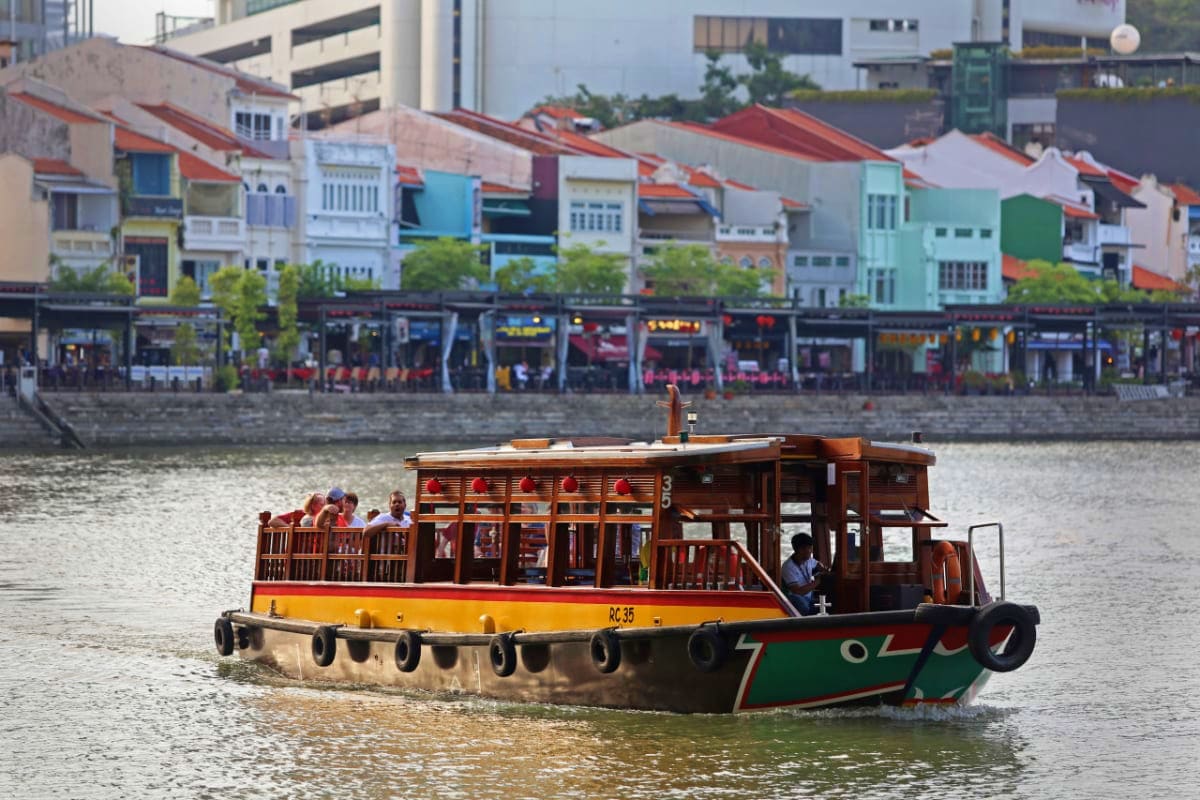 Traditional wooden river boat with passengers cruising past colorful shophouses along Singapore waterfront district