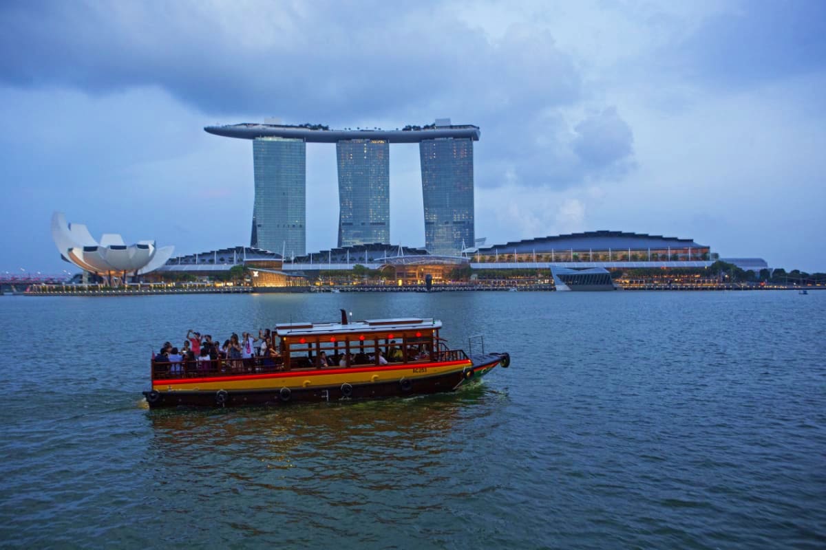Red and yellow traditional boat on Singapore River with Marina Bay Sands hotel and ArtScience Museum in background
