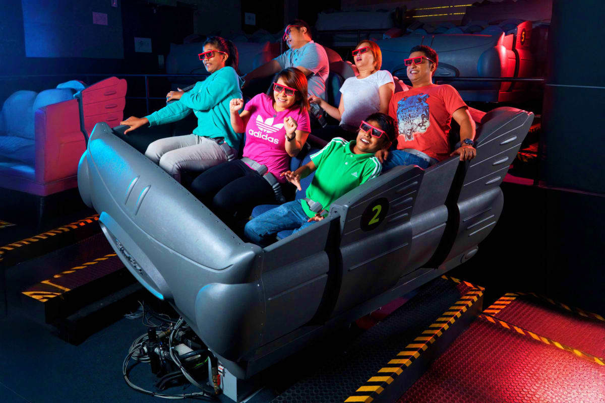 Group of people wearing 3D glasses riding a dynamic motion simulator ride with blue and red neon lighting at Sentosa 4D Adven