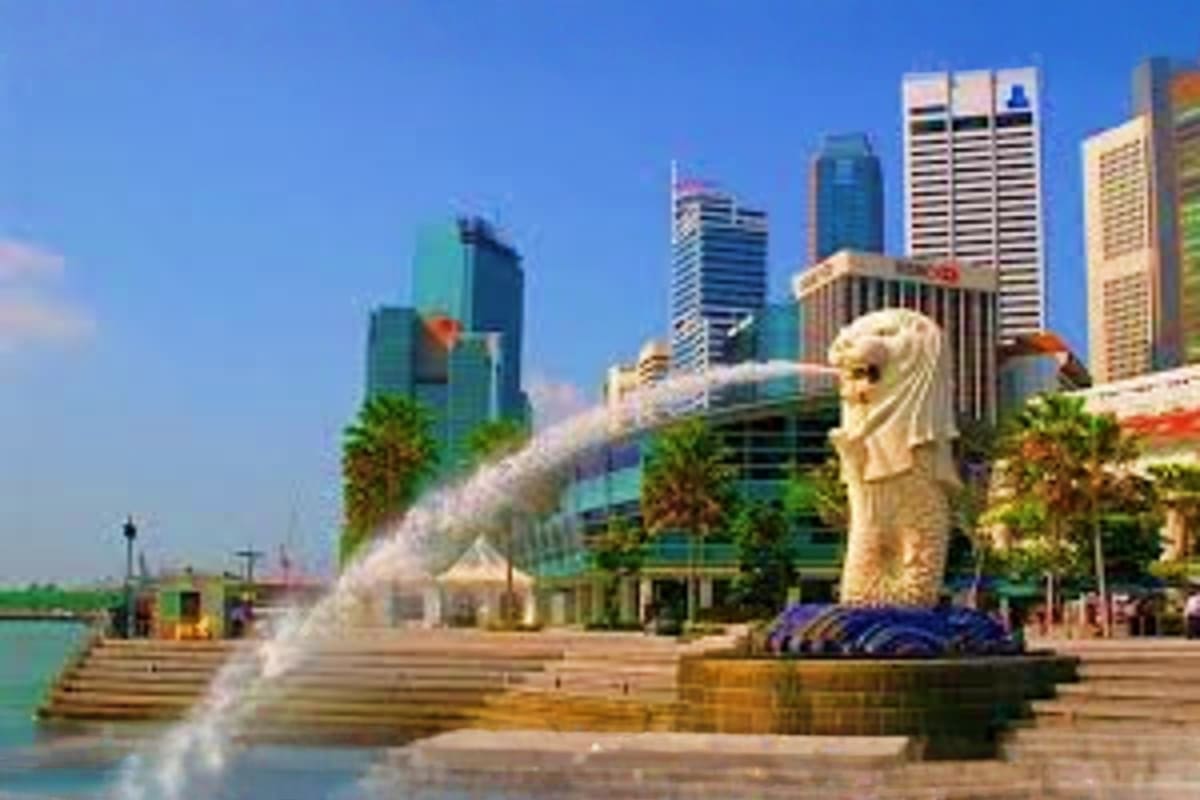 Merlion statue with water fountain spray in Singapore's Marina Bay with modern skyscrapers and palm trees in background