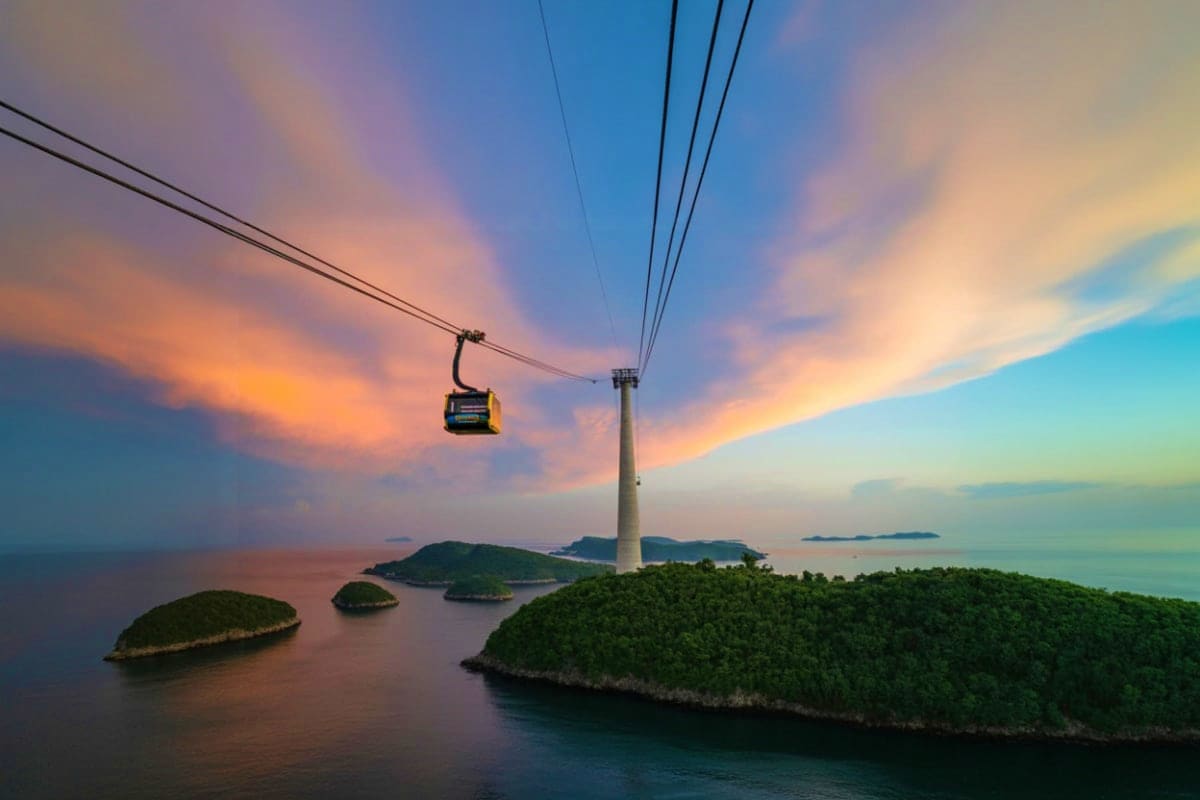 Yellow cable car suspended over turquoise sea with white tower and forested islands at sunset in Vietnam