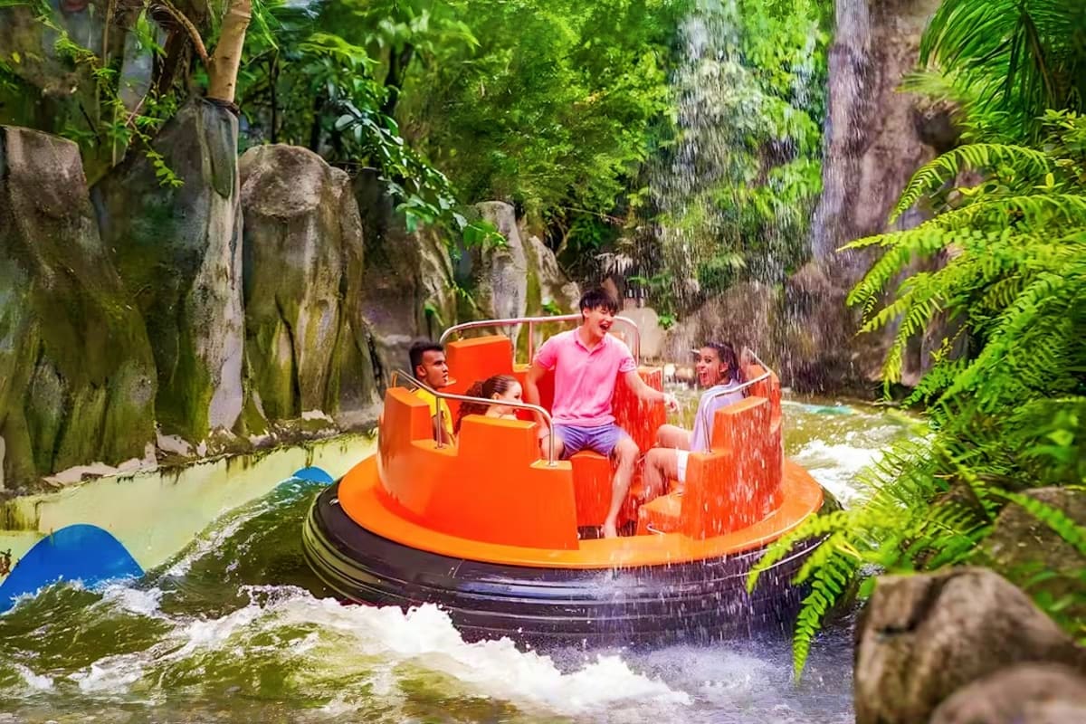 Family enjoying orange water ride boat at Sunway Lagoon theme park with lush green jungle foliage and water splash